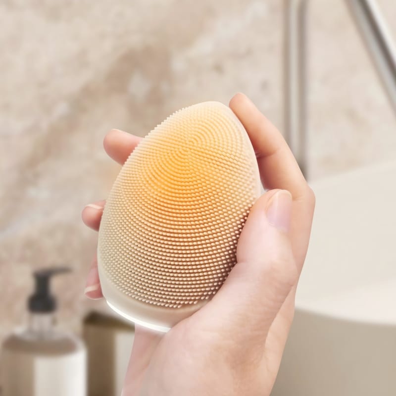 Hand holding the NICEMAY MR-1969 silicone facial brush in a bathroom setting.